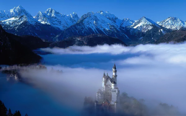 HD wallpaper of Neuschwanstein Castle emerging from fog with a backdrop of snow-capped mountains.