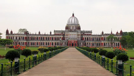 HD wallpaper of the man-made Cooch Behar Palace, showcasing its grand architecture and surrounding gardens under a cloudy sky.