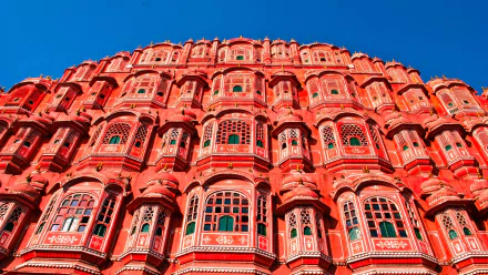 A vibrant HD wallpaper showcasing the intricate façade of Hawa Mahal, the iconic palace in Jaipur, India, featuring its beautiful red sandstone and numerous ornate windows against a clear blue sky.