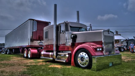 HD desktop wallpaper featuring a Kenworth semi-truck parked on grass under a cloudy sky, showcasing its polished chrome and classic design.