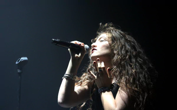 Curly-haired singer performing passionately on stage, holding a microphone under a dramatic spotlight — 5K Ultra HD PC desktop wallpaper, music concert scene.