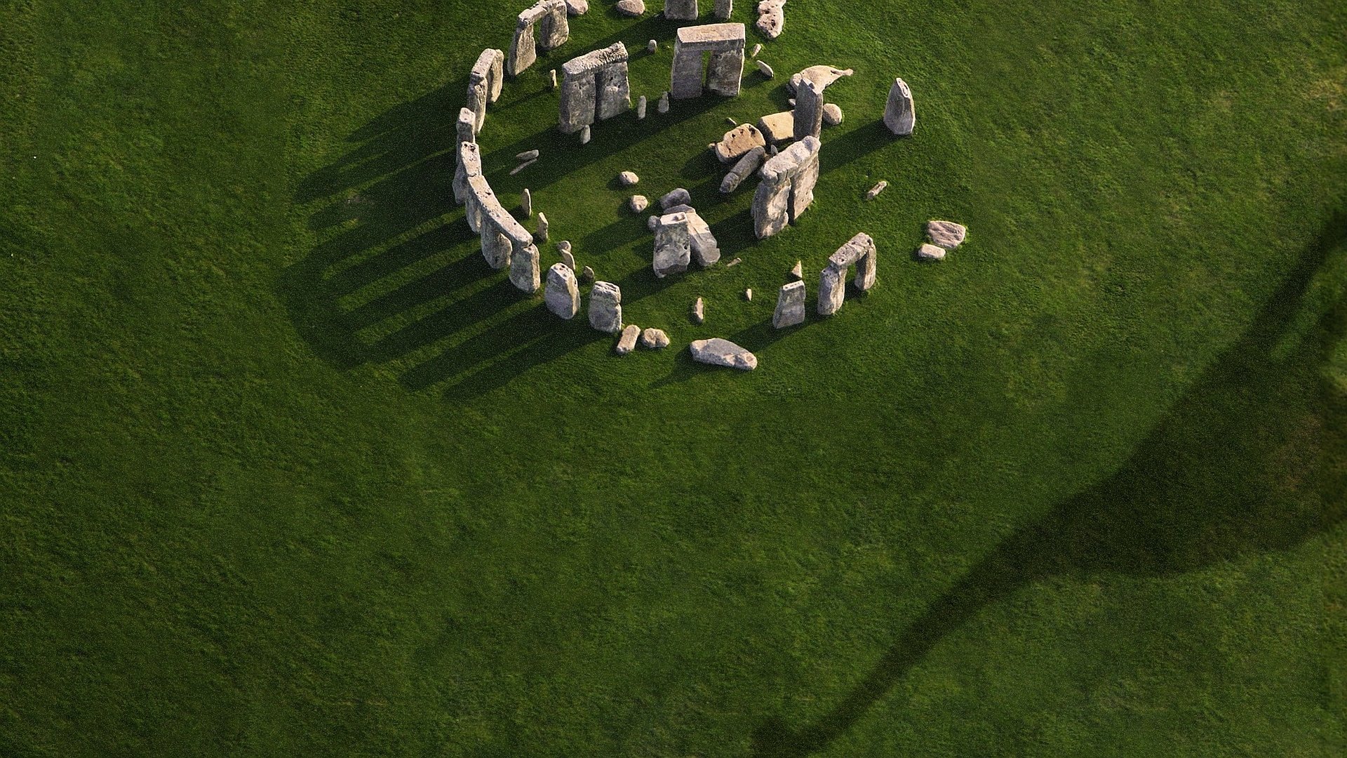 HD PC desktop wallpaper featuring a scene from the movie Jurassic World with ancient stone structures casting long shadows on green grass.