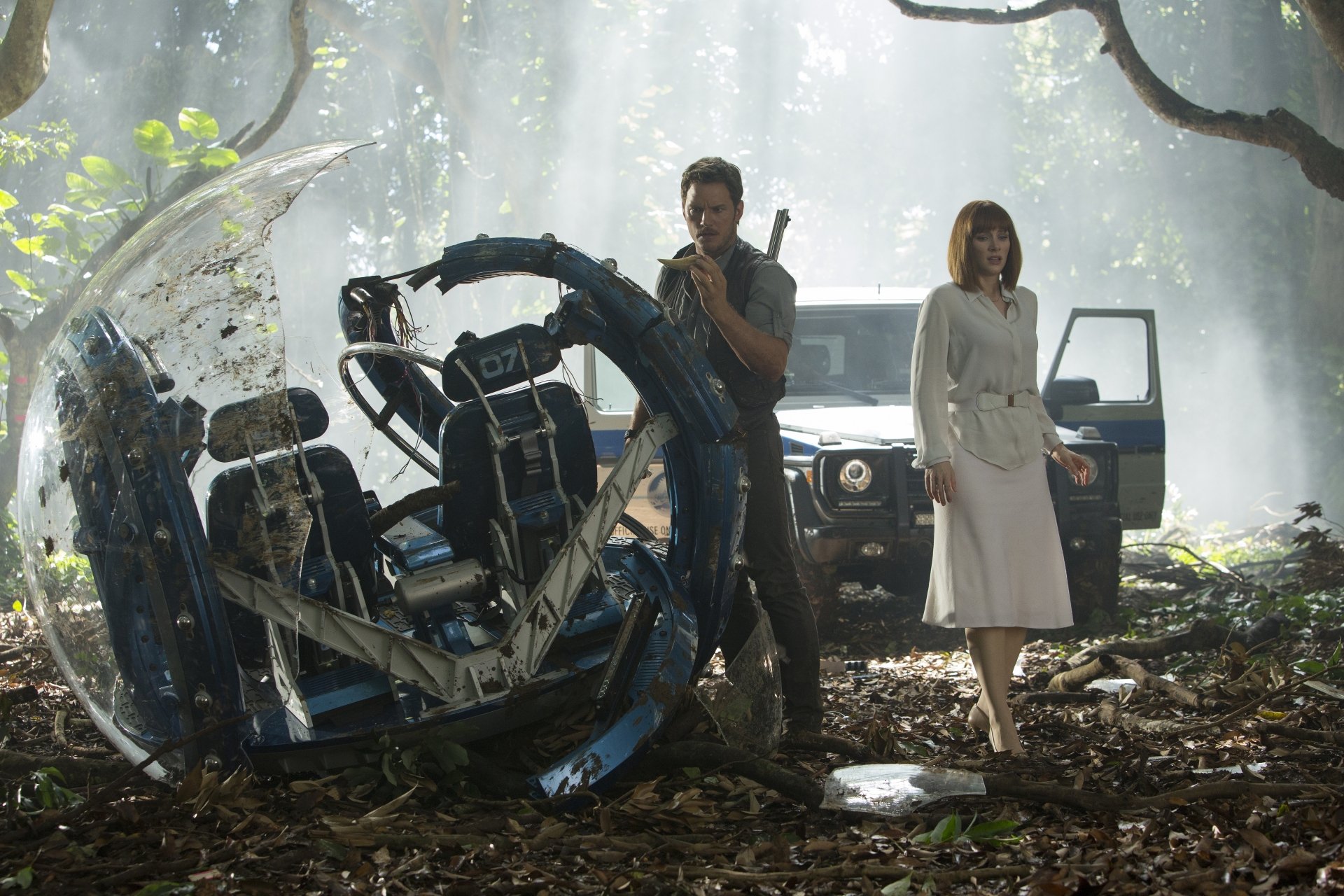 Bryce Dallas Howard and Chris Pratt stand in a lush jungle setting, with a damaged vehicle in the foreground, capturing a moment from the movie Jurassic World. High-definition wallpaper.