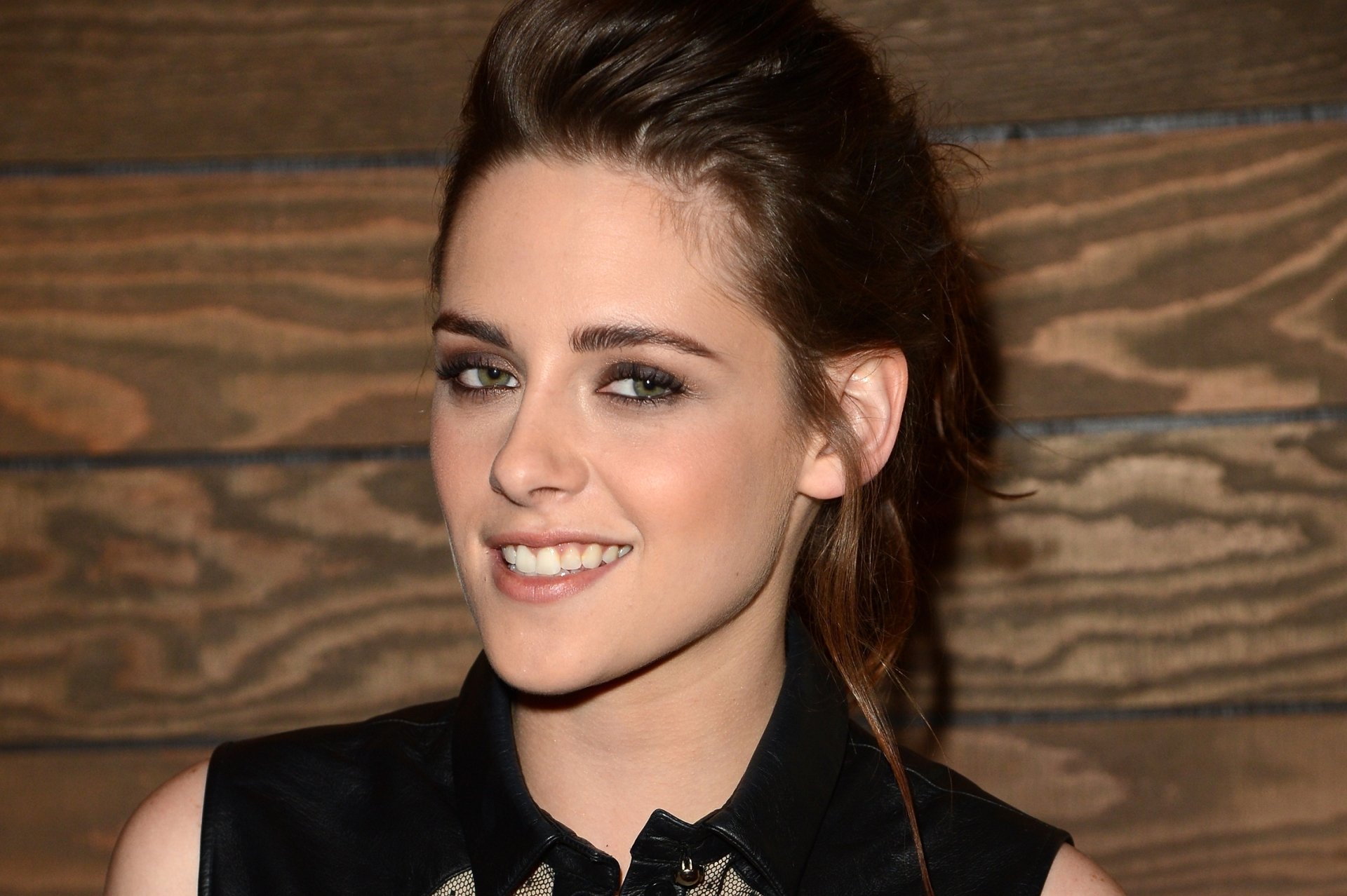 HD PC desktop wallpaper featuring a smiling Kristen Stewart against a wooden background, highlighting her natural look and casual style.