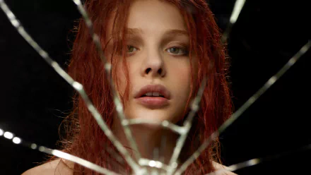 A striking HD wallpaper featuring Chloë Grace Moretz from the movie *Carrie* (2013), showcasing her intense gaze through a shattered mirror backdrop.