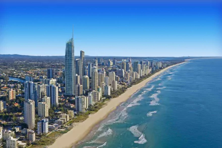 A stunning aerial view of the Gold Coast, Queensland, showcasing a vibrant skyline against a clear blue sky, with sandy shores and gentle waves lapping at the coast.