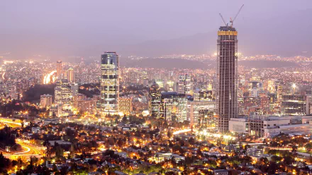 A 4K Ultra HD view of Santiago, Chile at dusk, showcasing the city's illuminated skyline and a tall man-made skyscraper under construction.