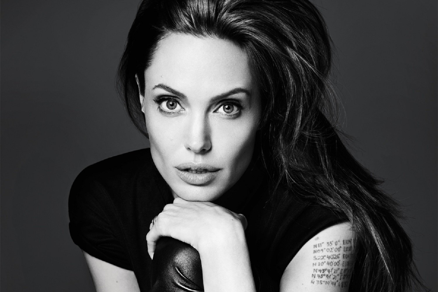Black and white HD desktop wallpaper featuring a close-up portrait of celebrity Angelina Jolie with intense gaze and visible tattoo on her arm.