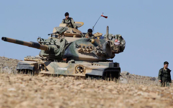 Military M60 Patton tank with crew advancing across rocky terrain under a clear sky — HD PC desktop wallpaper/background.
