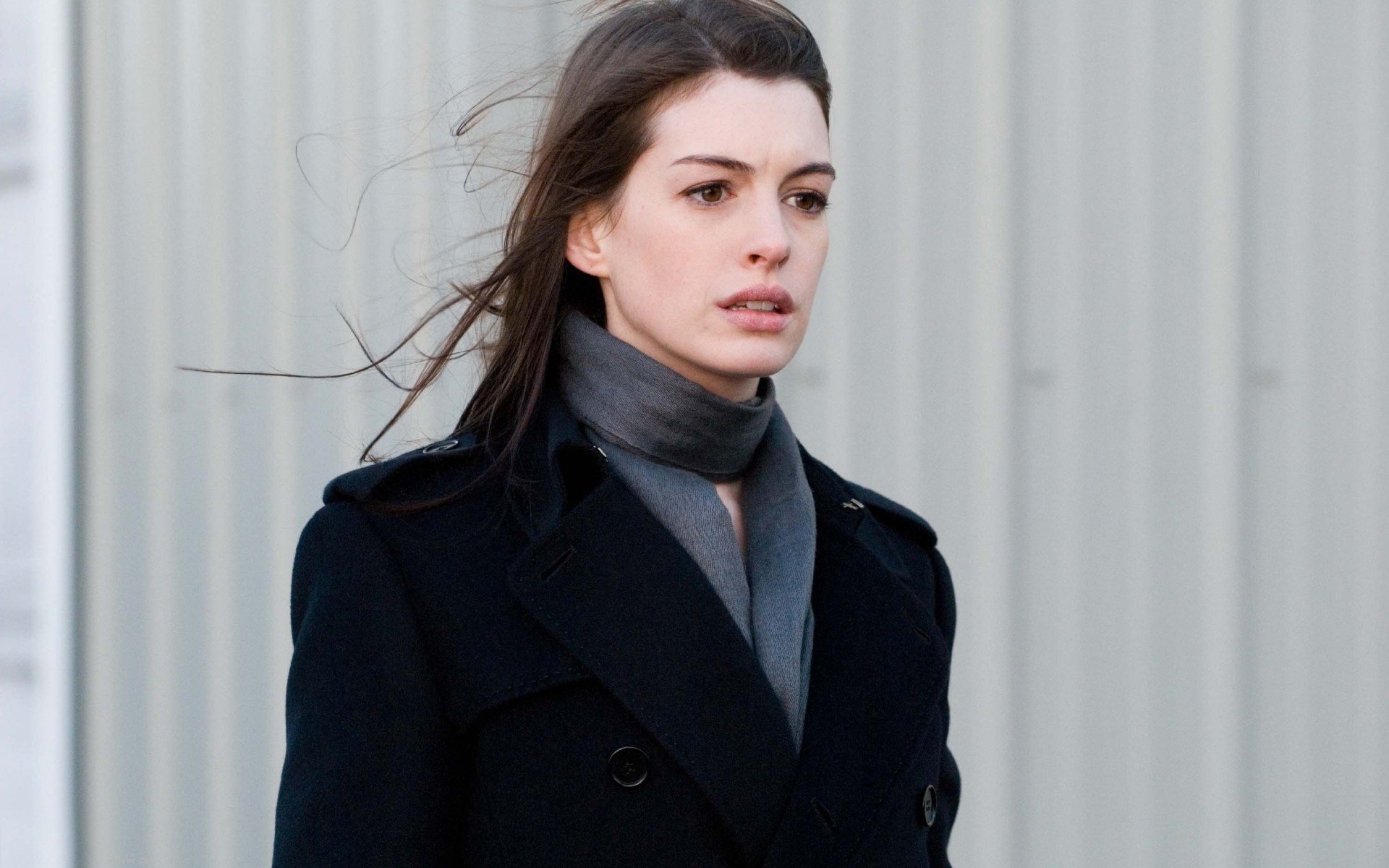 HD desktop wallpaper of celebrity Anne Hathaway wearing a dark coat and scarf with a neutral expression against a light, textured background.