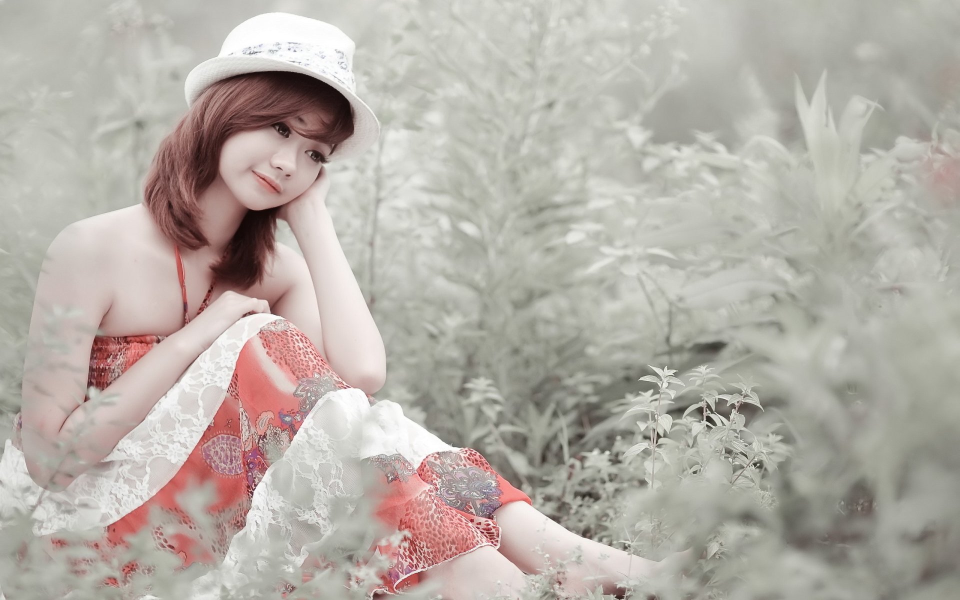 A serene Asian woman in a vibrant dress and hat sits in a lush green setting, captured as a beautiful high-definition desktop wallpaper and background.
