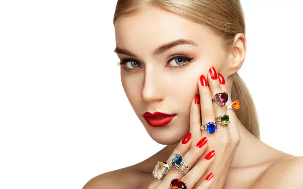 A woman with striking features and bold red nails gently touches her face while showcasing colorful rings. This 4K Ultra HD portrait highlights elegant jewelry and beauty.