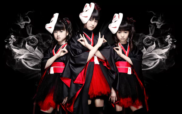 Three female metal idols, dressed in black and red outfits with traditional Japanese elements, pose against a dark background, embodying the vibrant energy of Babymetal in a heavy metal theme.