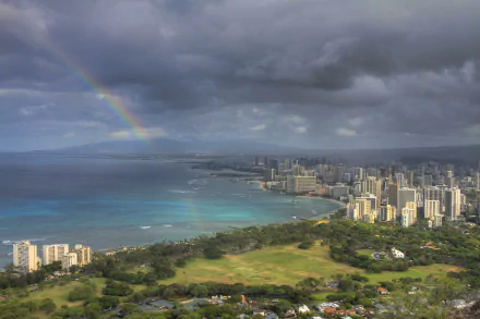 5K Ultra HD wallpaper of Honolulu and Waikiki on Oahu, Hawaii — a man-made skyline beside a turquoise bay under storm clouds with a bright rainbow.