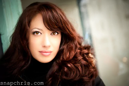 Close-up portrait of a woman with long auburn curls and a warm gaze, face-centered in a soft-lit scene — 4K Ultra HD PC desktop wallpaper/background.