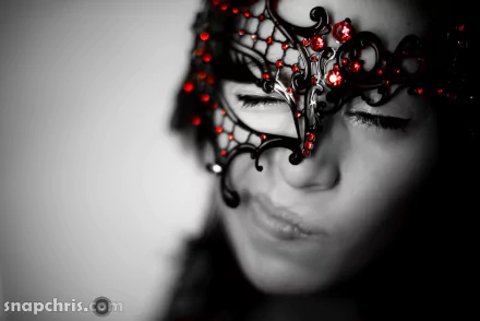 Close-up photography of a face wearing an ornate black filigree mask with red beads, moody grayscale background — 5K Ultra HD PC desktop wallpaper/background.