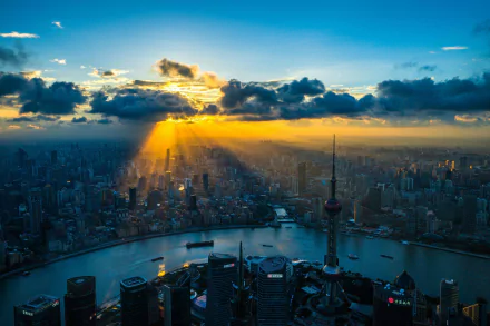 HD desktop wallpaper showcasing a stunning Shanghai cityscape at sunset, with vibrant rays breaking through clouds over the urban landscape and river.