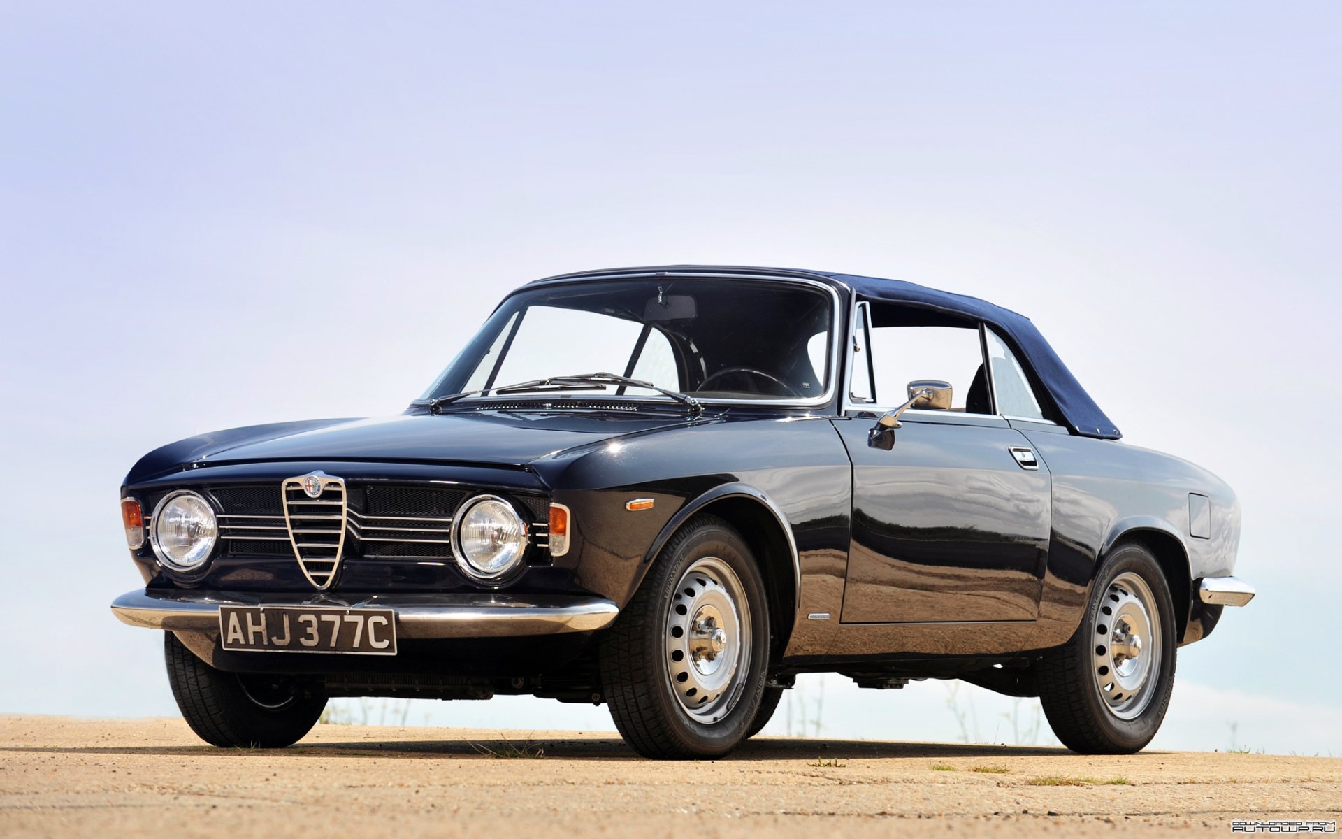 HD PC desktop wallpaper showing a classic black Alfa Romeo coupe parked on sunlit pavement under a pale blue sky.