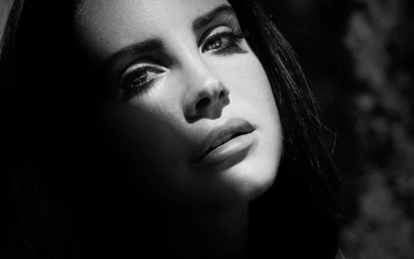 Black and white HD desktop wallpaper of Lana Del Rey with soft lighting highlighting her face against a dark, blurred background, evoking a moody musical atmosphere.