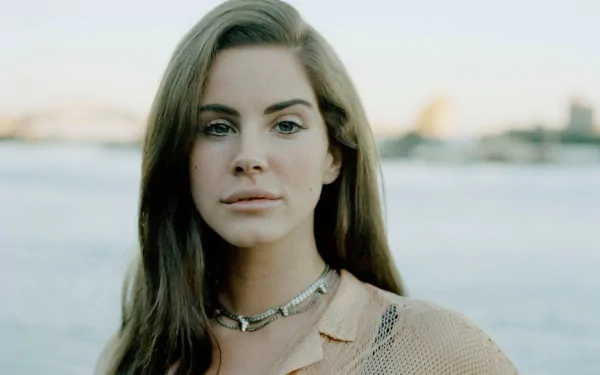 HD desktop wallpaper featuring a close-up portrait of Lana Del Rey against a soft, blurred outdoor background, evoking a serene and musical vibe.