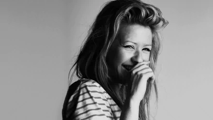 A black and white HD desktop wallpaper featuring Ellie Goulding smiling and playfully covering her mouth, embodying a joyful and carefree spirit.