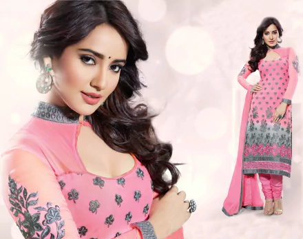 A glamorous Indian model showcases a stunning national dress in vibrant pink and gray, featuring intricate embroidery, set against a soft, blurred background.