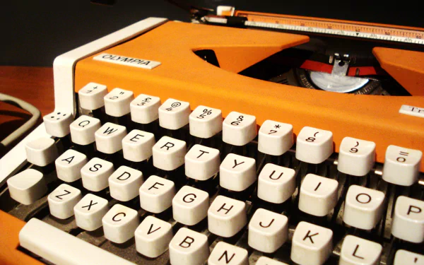 HD PC desktop wallpaper featuring a close-up of a vintage orange man-made typewriter with white keys under warm lighting.