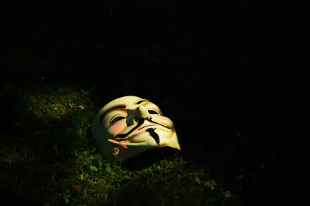 HD desktop wallpaper featuring an anonymous mask, symbolizing technology and anonymity, lying on the grass in a dimly lit environment.