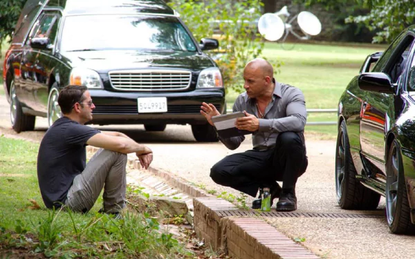 Vin Diesel interacts with a co-star in a scene from Furious 7, surrounded by luxury cars. This HD wallpaper captures an intense moment from the action-packed film.