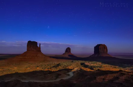 HD desktop wallpaper of Monument Valley's desert landscape in Utah under a starry night sky, showcasing natural rock formations and expansive open terrain.