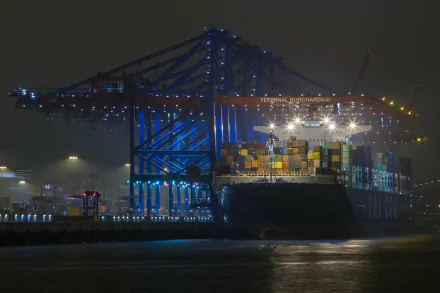 A brightly lit container ship docked at night, showcasing colorful cargo containers and illuminated cranes, serving as a striking HD desktop wallpaper and background.