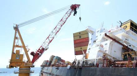 A vibrant HD wallpaper featuring a container ship being loaded with colorful cargo, showcasing a busy dock scene with a crane in action against a clear sky.