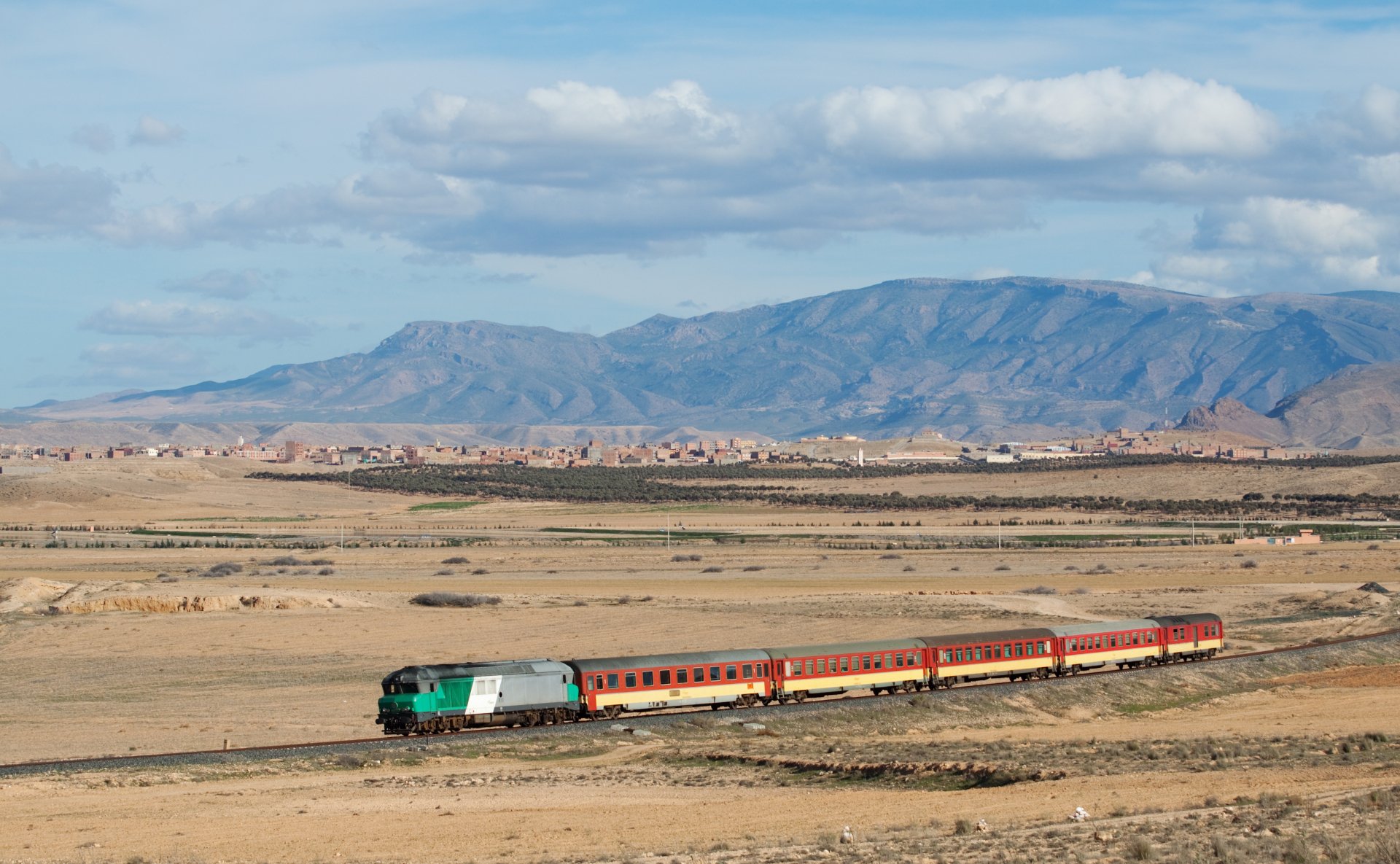4K Ultra HD desktop wallpaper of a colorful train traveling through a vast desert landscape with distant mountains under a partly cloudy sky.