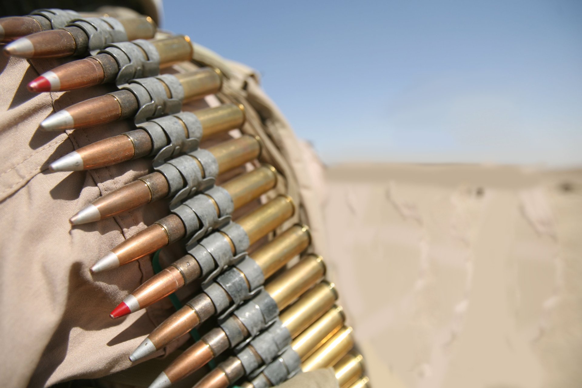 Close-up of man-made bullets linked together, displayed against a blurred desert background; an HD PC desktop wallpaper and background with sharp detail.