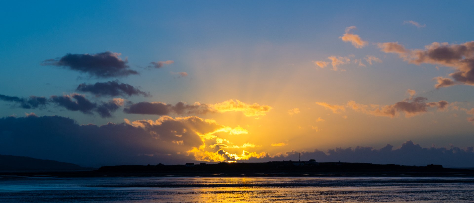 HD desktop wallpaper of a yellow sunset over an island with clouds scattered across the sky, reflecting on calm water below.