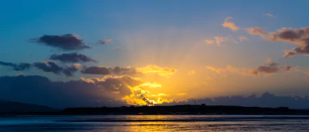HD desktop wallpaper of a yellow sunset over an island with clouds scattered across the sky, reflecting on calm water below.