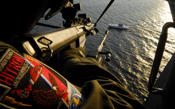 A dramatic HD desktop wallpaper showcasing the perspective of a Coast Guard member during an operation, with a vessel visible on the shimmering water below.