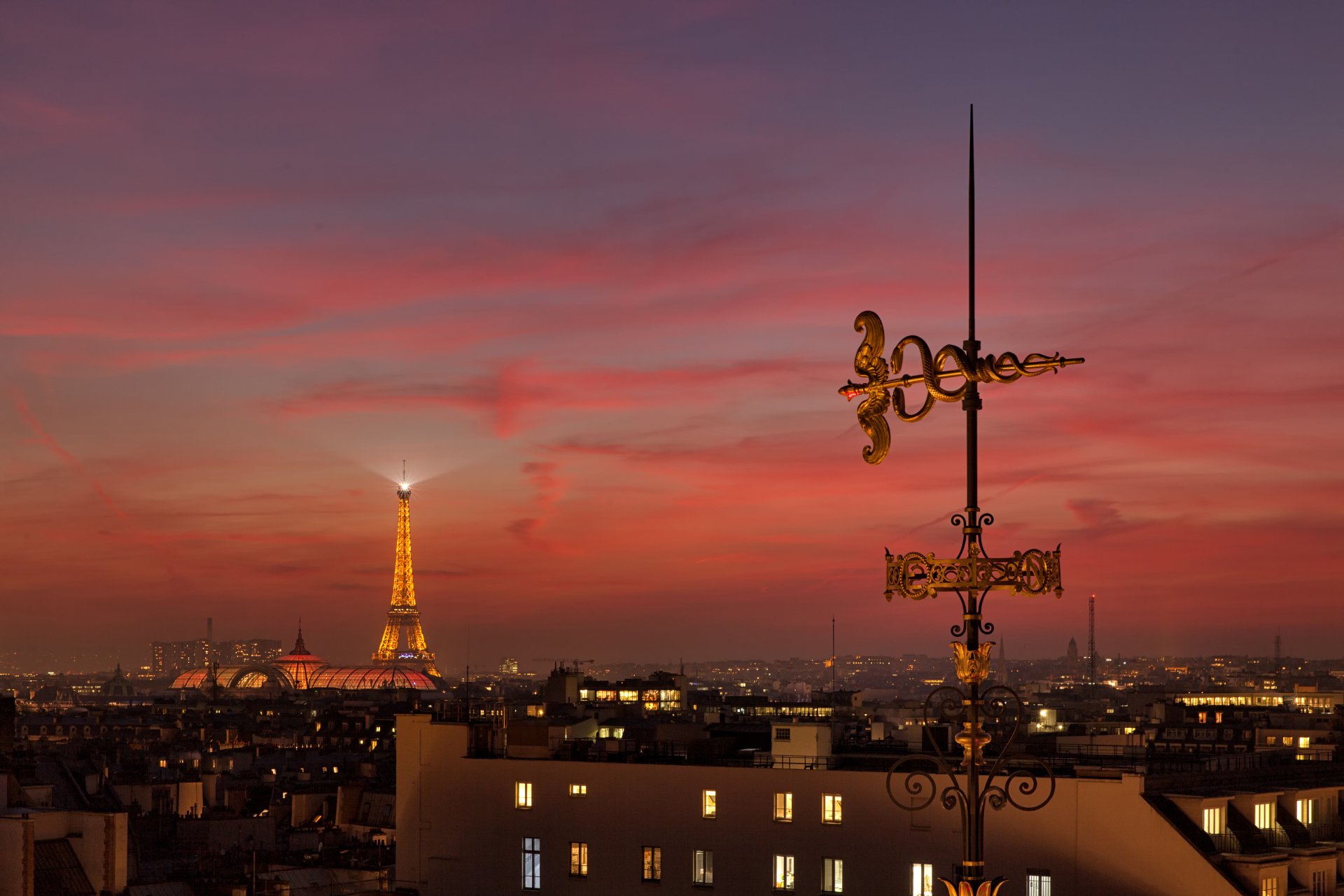 4K Ultra HD wallpaper of the Eiffel Tower glowing at twilight against a vibrant Paris sunset with city rooftops and an ornate weather vane in the foreground.