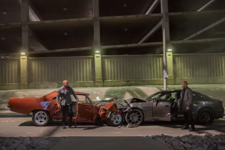 A HD desktop wallpaper featuring Jason Statham as Deckard Shaw and Vin Diesel as Dominic Toretto from Furious 7, standing beside two crashed cars in a dimly lit parking garage.