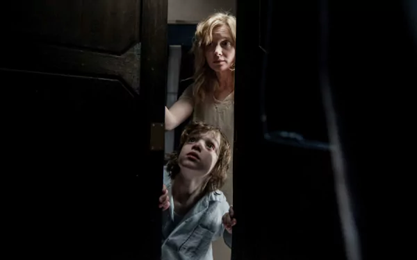 Essie Davis and Noah Wiseman in a dark, tense scene from the movie The Babadook, featured in a 4K Ultra HD PC desktop wallpaper and background.