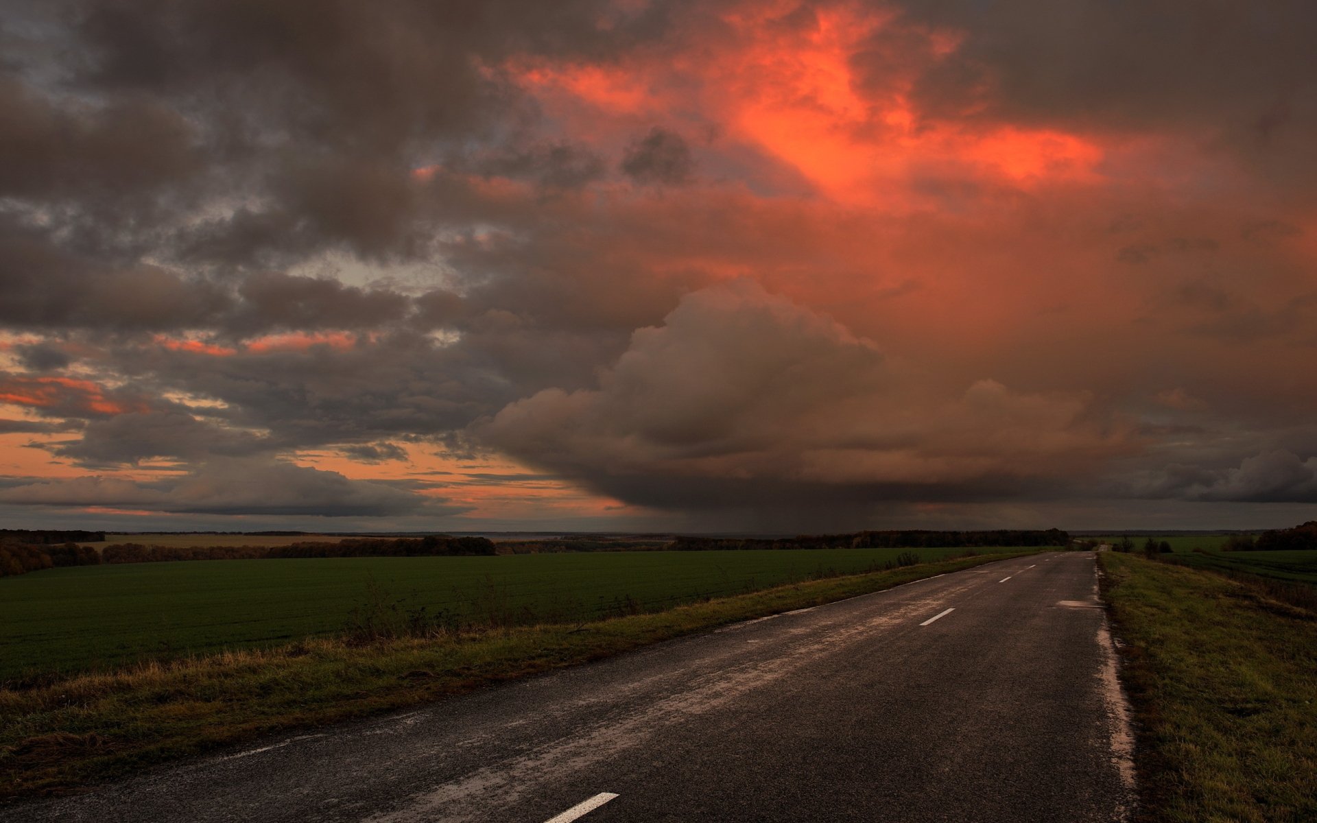 HD desktop wallpaper showcasing a dramatic storm over an open road with dark clouds and a fiery orange sky in a natural landscape.