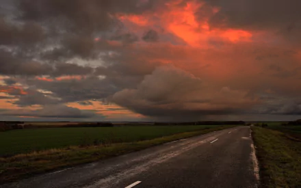 HD desktop wallpaper showcasing a dramatic storm over an open road with dark clouds and a fiery orange sky in a natural landscape.