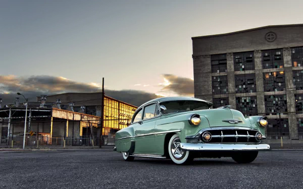 HD PC desktop wallpaper: mint-green classic Chevrolet vehicle parked in an industrial lot at dusk, chrome details and a dramatic sky.