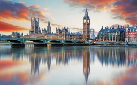 4K Ultra HD image of Buckingham Palace and the Palace of Westminster, with Big Ben and Westminster Bridge reflected in the River Thames under a vibrant sunset sky.