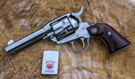A Ruger New Vaquero revolver rests on a wooden surface, accompanied by a lighter. This 4K Ultra HD image captures the detail of the firearm against its natural backdrop.