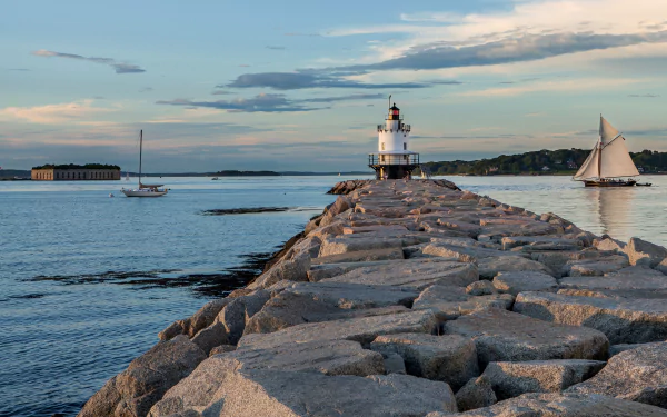 4K Ultra HD PC desktop wallpaper of a man-made lighthouse on a rocky jetty with sailboats on calm coastal waters at sunset.