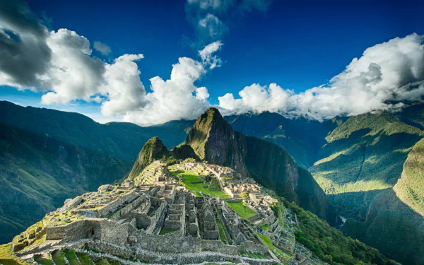Stunning 4K Ultra HD image of the man-made ancient ruins of Machu Picchu set against a dramatic mountainous background under a cloudy sky.