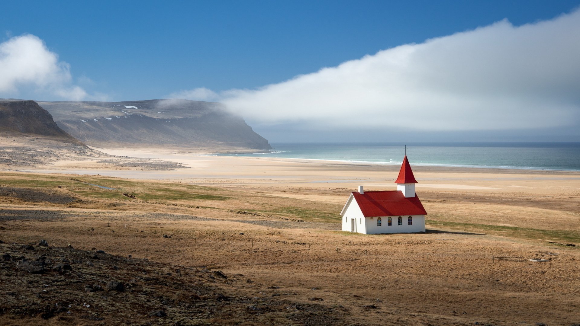 HD PC desktop wallpaper featuring a solitary church with a red roof on a vast, sandy landscape under a clear blue sky, evoking a peaceful religious atmosphere.