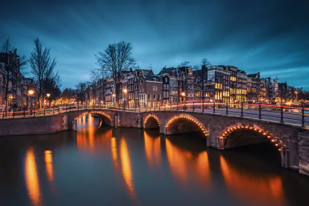 Evening view of Amsterdam's Emperor's Canal, showcasing illuminated buildings reflecting on the water, with softly lit bridges enhancing the serene cityscape.