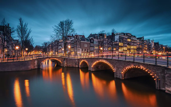 Evening view of Amsterdam's Emperor's Canal, showcasing illuminated buildings reflecting on the water, with softly lit bridges enhancing the serene cityscape.